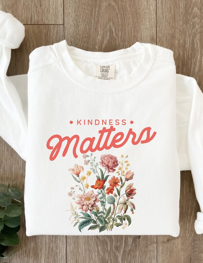 May include: White long-sleeve sweatshirt with the text "KINDNESS MATTERS" in pink lettering and a floral design in shades of pink, red, yellow, and green.