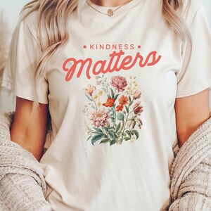 May include: A white t-shirt with a floral design and the text "KINDNESS MATTERS" in pink lettering.