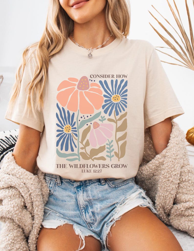 May include: A beige t-shirt with a floral design and the text "Consider How The Wildflowers Grow Luke 12:27".