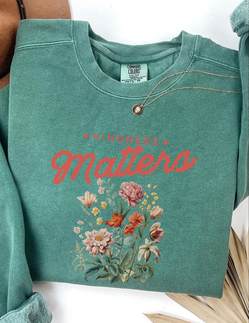 May include: Teal green sweatshirt with the text "Kindness Matters" in red lettering and a floral design.