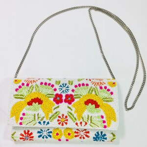Pu&ograve; includere: Una pochette bianca in perle con una tracolla a catena argentata. La borsa &egrave; decorata con ricami floreali colorati.
