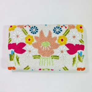 Pu&ograve; includere: Una pochette bianca di perline con un motivo floreale. I fiori sono rosa, arancio, giallo, verde e blu.