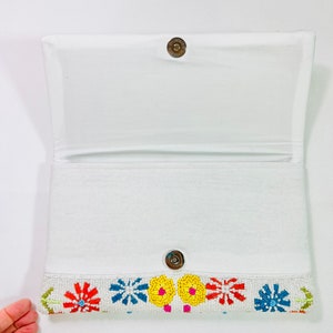 Pu&ograve; includere: Clutch bianca con perline e un design floreale. I fiori sono in tonalit&agrave; di giallo, rosso, blu e verde.