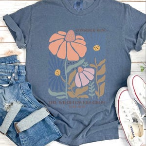 May include: A blue t-shirt with a floral design and the text "Consider how the wildflowers grow".