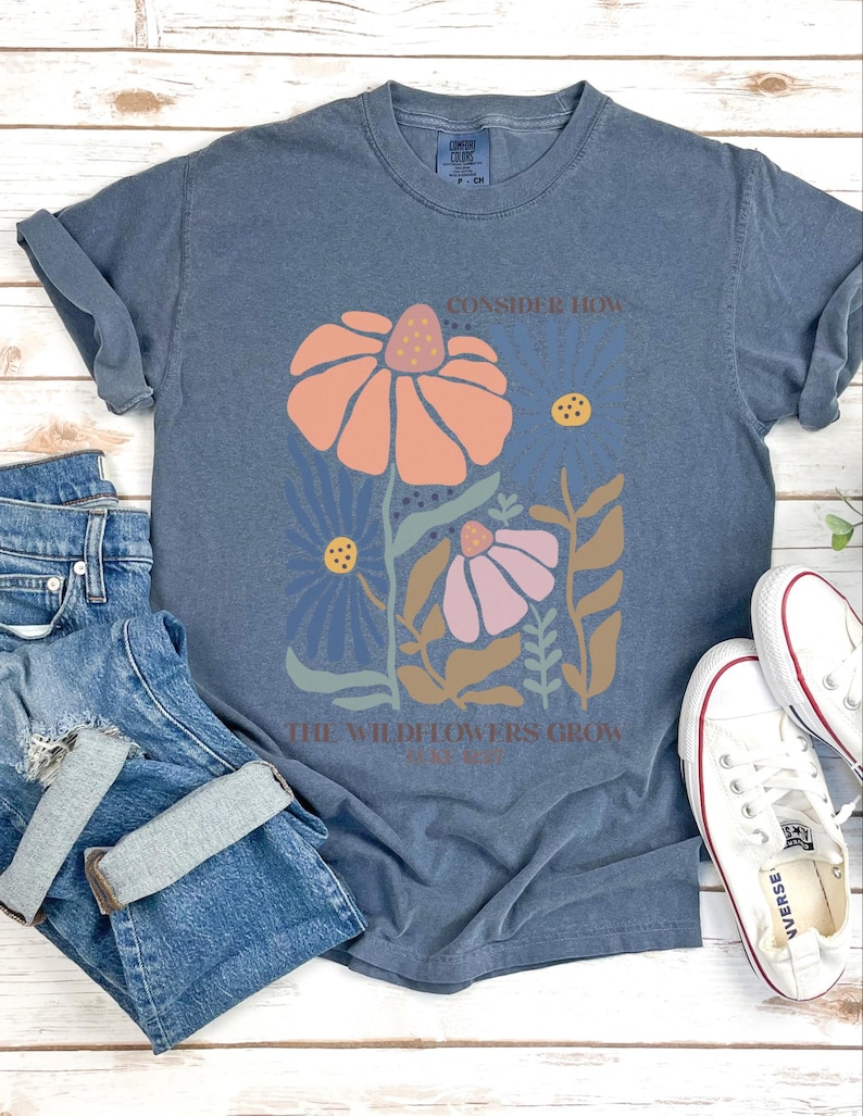 May include: A blue t-shirt with a floral design and the text "Consider how the wildflowers grow".