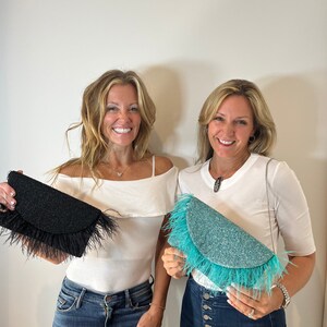 May include: Two women are holding feather-trimmed clutches. One clutch is black with black feathers, and the other is turquoise with turquoise feathers.