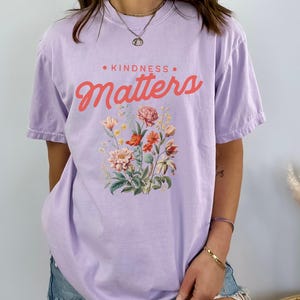 May include: A lavender t-shirt with a floral print and the text "KINDNESS MATTERS" in pink.