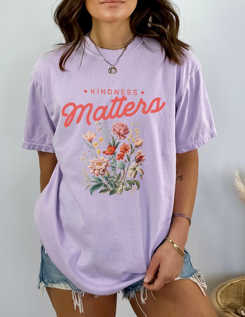 May include: A lavender t-shirt with a floral print and the text "KINDNESS MATTERS" in pink.