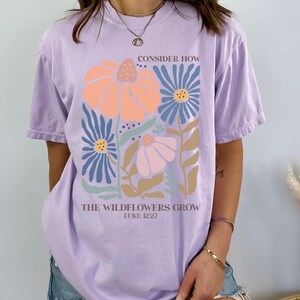 May include: A lavender t-shirt with a floral design and the text "Consider how the wildflowers grow, Luke 12:27".