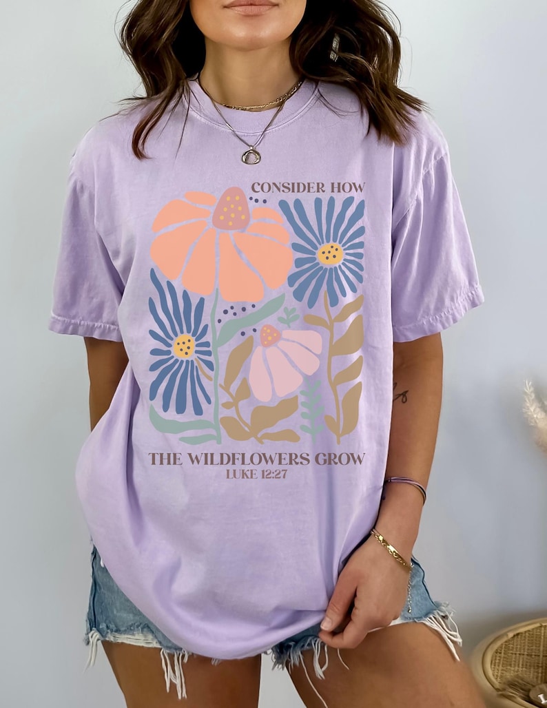 May include: A lavender t-shirt with a floral design and the text "Consider how the wildflowers grow, Luke 12:27".