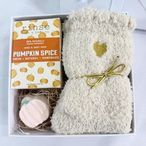 Pode incluir: Um conjunto de presente numa caixa branca, com uma barra de sabonete Pumpkin Spice, uma meia de pelúcia creme e uma bomba de banho rosa. A caixa de sabonete diz "Pumpkin Spice" e "98% Naturally Derived Ingredients". A meia tem um coração e um laço dourados.