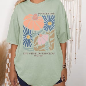 May include: A light green oversized t-shirt with a floral design and the text "Consider how the wildflowers grow Luke 12:27".