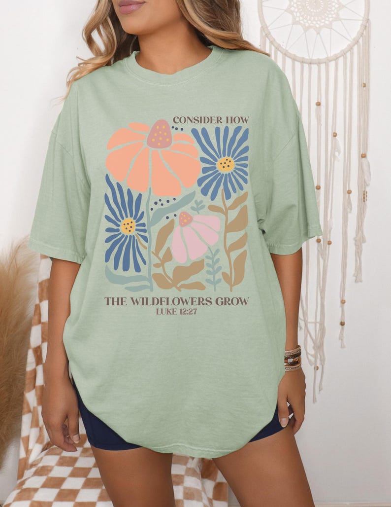 May include: A light green oversized t-shirt with a floral design and the text "Consider how the wildflowers grow Luke 12:27".
