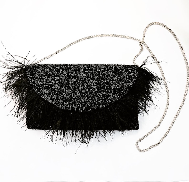 May include: A black beaded clutch with a feather trim and a silver chain strap.