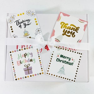 May include: Four greeting cards with different designs. The first card is white with yellow dots and flowers and says "Thinking of You". The second card is pink with gold lettering and says "Thank You". The third card is white with a pink, green, and purple border and says "Happy Birthday". The fourth card is white with a green border and says "Merry Christmas!"