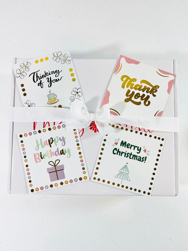 May include: Four greeting cards with different designs. The first card is white with yellow dots and flowers and says "Thinking of You". The second card is pink with gold lettering and says "Thank You". The third card is white with a pink, green, and purple border and says "Happy Birthday". The fourth card is white with a green border and says "Merry Christmas!"
