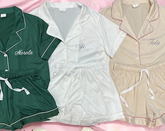 May include: Three sets of pajamas in green, white, and beige with short sleeves and matching shorts. Each set has a different name embroidered on the top: Morola, Ife, and Tola.