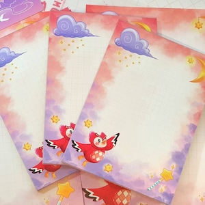 May include: A set of four pink and purple notepads with a grid pattern. Each notepad features a whimsical illustration of a red owl flying in a night sky with clouds, stars, and a crescent moon.