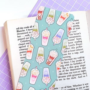 May include: A turquoise blue bookmark with a repeating pattern of colorful bubble tea cups with tapioca pearls. The bookmark is designed to look like a cartoon illustration.
