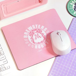 May include: A pink mouse pad with a white logo that says "Brewsters Roost - Est. 2005" and a white mouse on top of it.