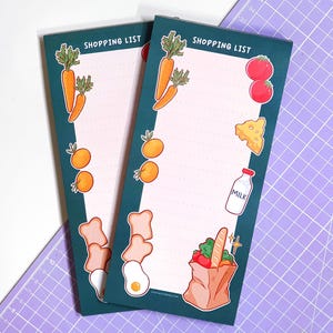 May include: Two rectangular shopping list notepads with a teal border and the words "SHOPPING LIST" at the top. The notepads feature illustrations of carrots, oranges, tomatoes, cheese, milk, bread, and a grocery bag.