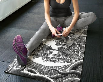 May include: A woman sits on a black and white yoga mat with a graphic print of a mythical creature. She is wearing gray leggings and a black tank top. She is looking down at her phone.