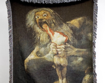 Può includere: Una coperta in tessuto a trama di arazzo che presenta una rappresentazione oscura e dettagliata di una figura grottesca con una bocca spalancata, che consuma una figura più piccola. La coperta ha un bordo a frangia.