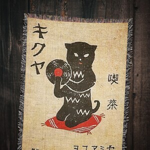 May include: A black cat holding a vinyl record with the Japanese text "キワヤ" and "ユアミセ" on a beige background with red and black accents.