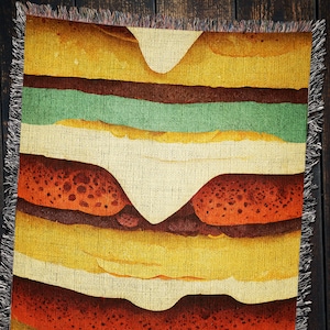 May include: A woven tapestry with a colorful design of a burger. The burger is made up of layers of red, yellow, and green fabric. The tapestry is a great way to add a touch of whimsy to your home decor.