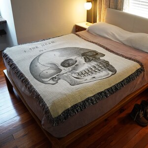 May include: A woven throw blanket with a black and white anatomical illustration of a human skull. The skull is labeled with numbers and the text "1 THE HEAD. FIG. 1."