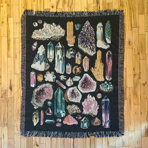May include: A tapestry featuring a variety of colorful crystals and gemstones on a black background. The tapestry is woven with intricate details and includes a variety of shapes and sizes of crystals.