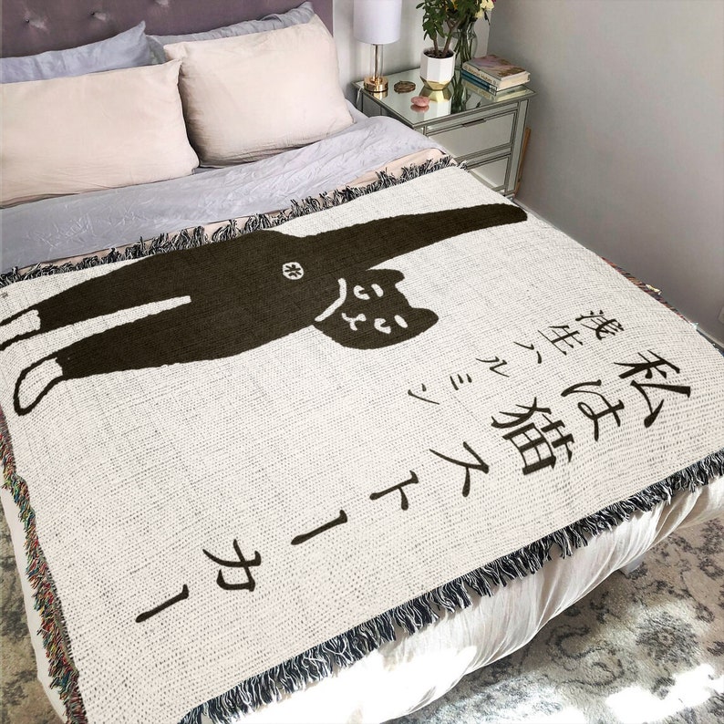 May include: A white throw blanket with a black cat illustration and Japanese text that reads "This cat is a little bit of a rascal".