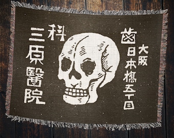 May include: A brown woven tapestry with a white skull and Japanese text. The text reads "三杯  東京電  院" and "大  阪  本  橋  五  丁目".