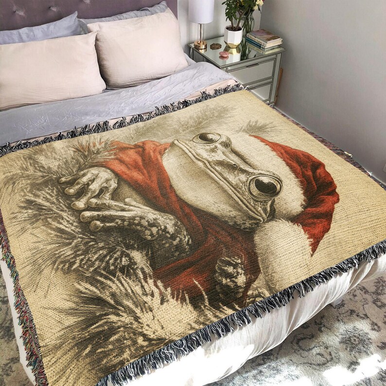 May include: A woven throw blanket featuring a close-up of a frog wearing a Santa hat. The frog is depicted in a realistic style with detailed features and a soft, fuzzy texture.