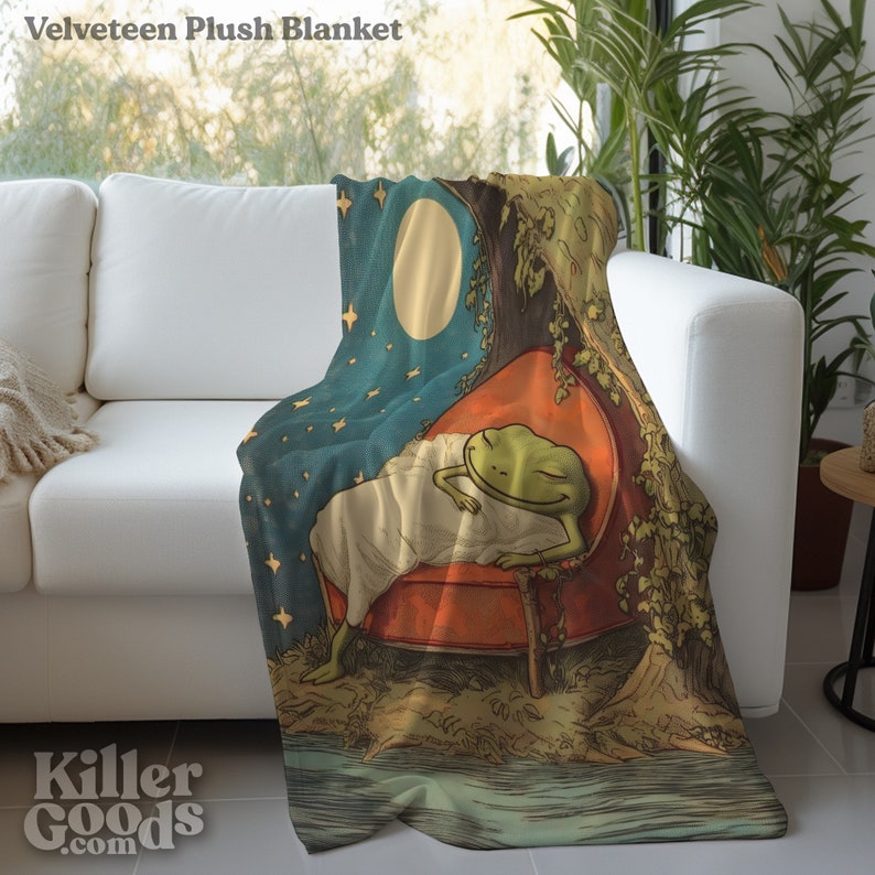 May include: A plush blanket featuring a green frog sleeping on a red chair under a tree with a full moon and stars in the sky. The blanket has a vintage illustration style.