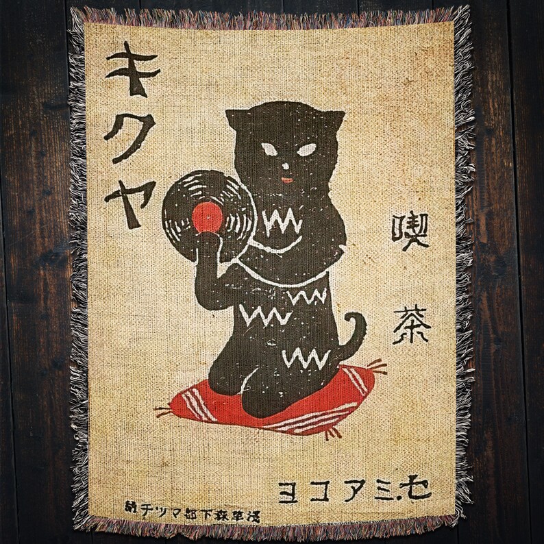 May include: A tan throw blanket with a black cat holding a vinyl record. The cat has a black and white pattern on its body. The text on the blanket reads "キクヤ" and "ヨコハマセ".