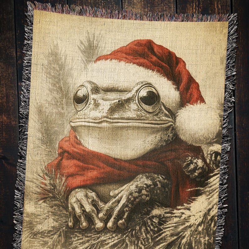 May include: A green frog wearing a red and white Santa hat and a red scarf. The frog is sitting in a pile of brown and white twigs.