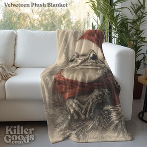May include: A plush blanket featuring a brown frog wearing a red Santa hat and scarf. The frog is sitting on a bed of brown and white fur. The blanket is made of soft, velvety material.