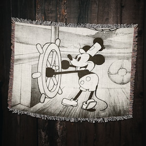 May include: Black and white woven tapestry featuring Mickey Mouse dressed as a sailor, holding a ship's wheel. The background shows a ship's interior with a life preserver.