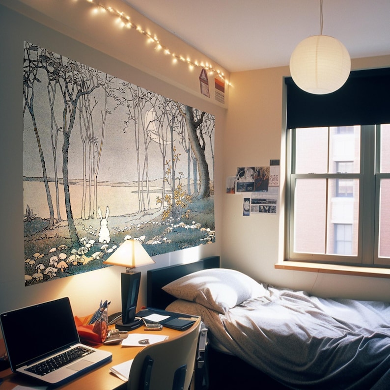 May include: A bedroom with a white bed, a desk with a laptop, and a large tapestry on the wall depicting a forest scene with a white rabbit. The tapestry is a light blue and gray color with a light pink sky. The room has a white ceiling with string lights and a white lampshade hanging from the ceiling.