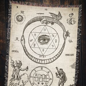 Puede incluir: Un tapiz con una ilustraci&oacute;n en blanco y negro de una serpiente mordi&eacute;ndose la cola, formando un c&iacute;rculo alrededor de una estrella de seis puntas con un ojo en el centro. El texto "OMNIA", "VNVS EST", "III", "&omicron;&upsilon;&rho;ά&beta;ό&rho;&omicron;&sigmaf;", "יהוה", y "Z" tambi&eacute;n se incluyen en el dise&ntilde;o.