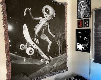 May include: Black and white tapestry depicting a skeleton alien skateboarding. The alien is wearing a black shirt and has a long, thin tail. The skateboard is a classic design with black wheels. The background is a dark, starry night.