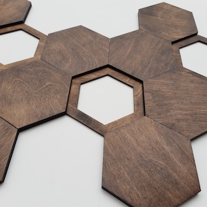 May include: A set of dark brown wooden hexagonal tiles arranged in a honeycomb pattern. The tiles are made of plywood and have a natural wood grain.