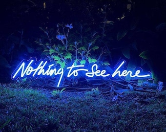 May include: A neon sign in a cursive font that reads "Nothing to see here" in white against a dark blue background. The sign is sitting on a patch of green grass.
