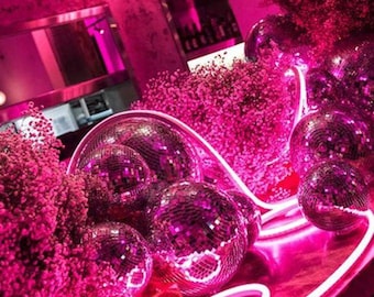 May include: Pink neon lights and disco balls in a pink room with pink flowers. The neon lights spell out "Chateau Am 22."