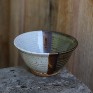 May include: A white and brown ceramic bowl with a speckled glaze. The bowl has a green and brown stripe around the rim.
