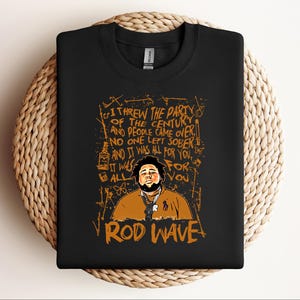 K&ouml;nnte beinhalten: Schwarzes Sweatshirt mit einer Grafik von Rod Wave und dem Text: "Ich habe die Party des Jahrhunderts geschmissen und die Leute kamen, niemand blieb n&uuml;chtern und es war alles f&uuml;r dich." Das Design ist orange.