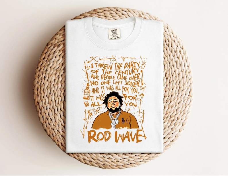 K&ouml;nnte beinhalten: Wei&szlig;es T-Shirt mit einer orangefarbenen Grafik von Rod Wave und Text. Der Text enth&auml;lt den Satz &bdquo;Ich habe die Party des Jahrhunderts geschmissen&ldquo; und &bdquo;Rod Wave&ldquo;. Das T-Shirt ist auf einer gewebten, kreisf&ouml;rmigen Oberfl&auml;che gefaltet.