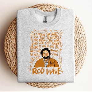 K&ouml;nnte beinhalten: Hellgraues Sweatshirt mit einer Grafik von Rod Wave und dem Text: "Ich habe die Party des Jahrhunderts geschmissen und die Leute kamen...und es war alles f&uuml;r dich." Das Design ist braun und orange.