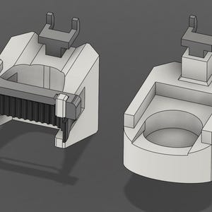 Peut inclure: Deux composants mécaniques gris clair imprimés en 3D. La pièce de gauche présente un mécanisme de serrage nervuré gris foncé avec un support en U sur le dessus. La pièce de droite est un bloc solide avec un centre circulaire évidé.